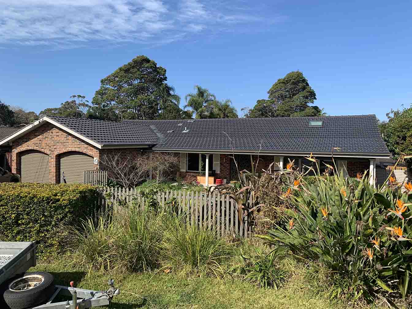 Brick home with a dark tiled roof behind a leafy garden