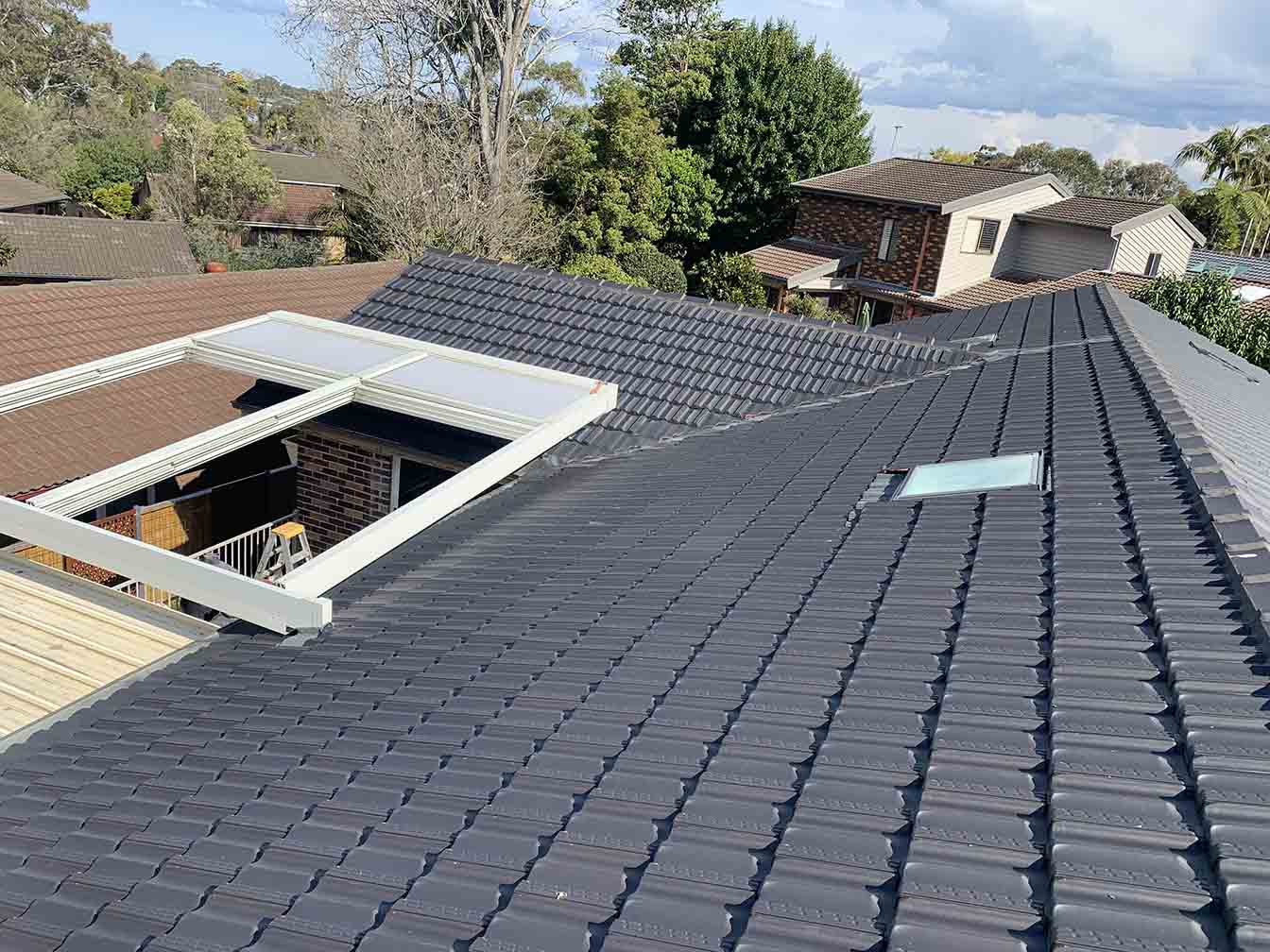 Dark grey tiled roof with a skylight beside a white pergola