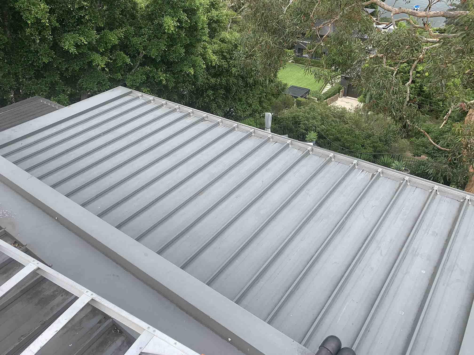 Light grey ribbed metal roof and box gutter overlooking treetops