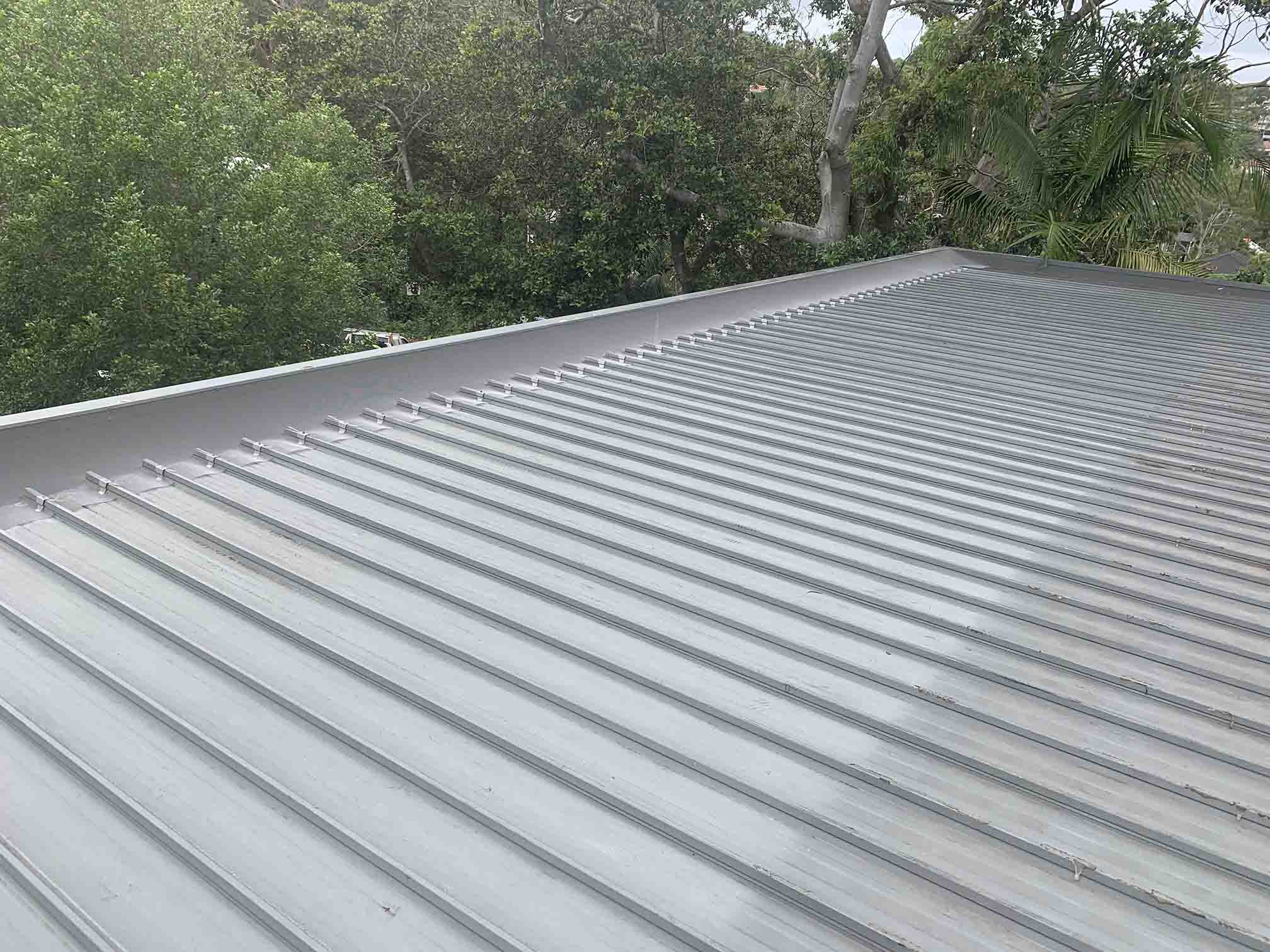 Long run of light grey ribbed metal roofing with trees behind