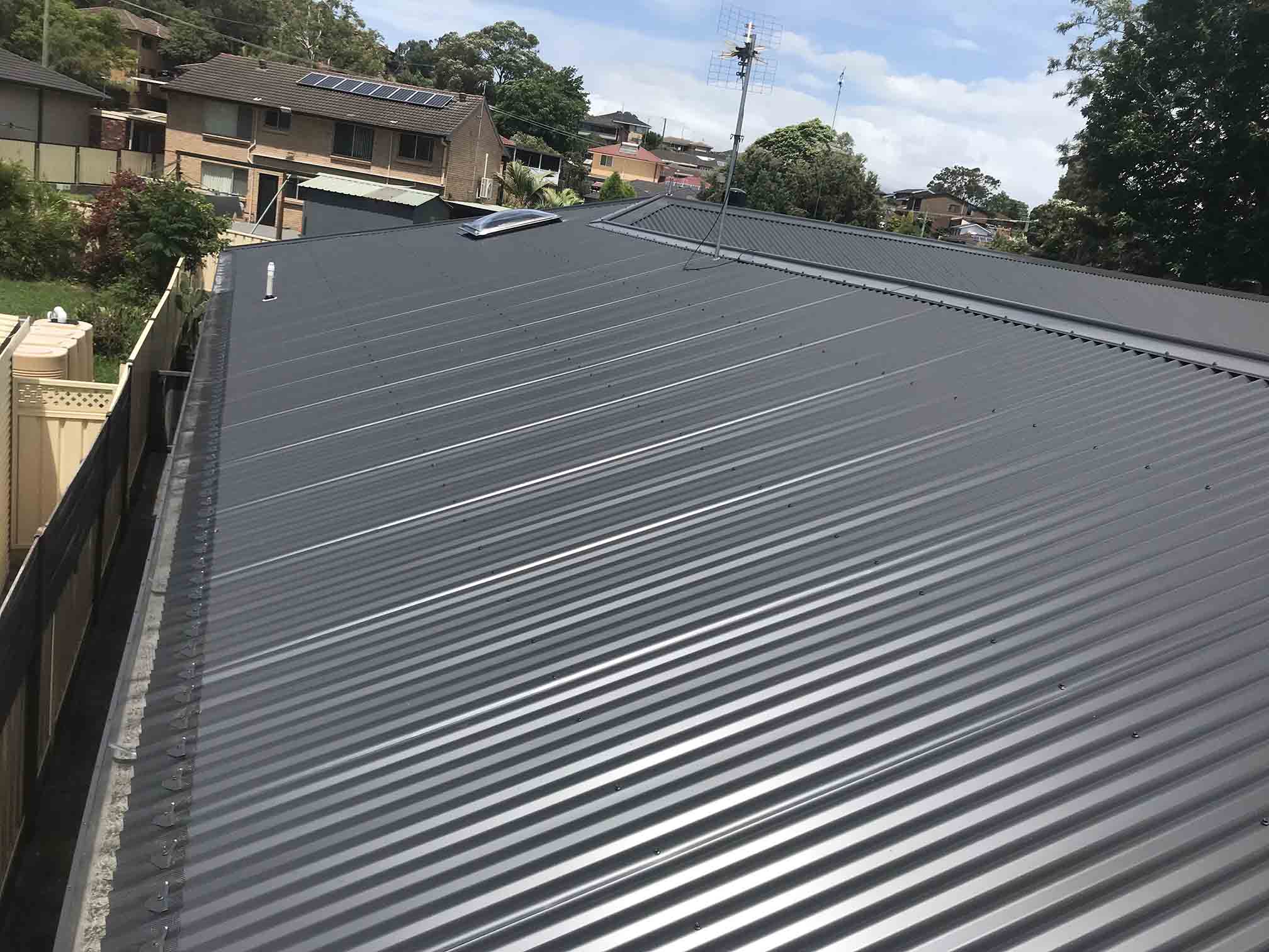 Long charcoal corrugated metal roof beside a timber fence