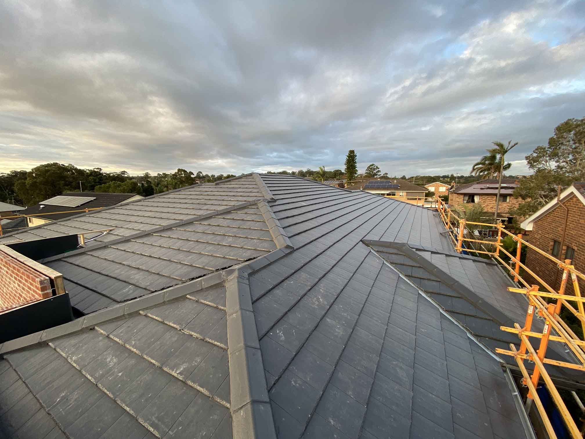 Grey tiled roof with orange scaffolding along the edge, cloudy sky