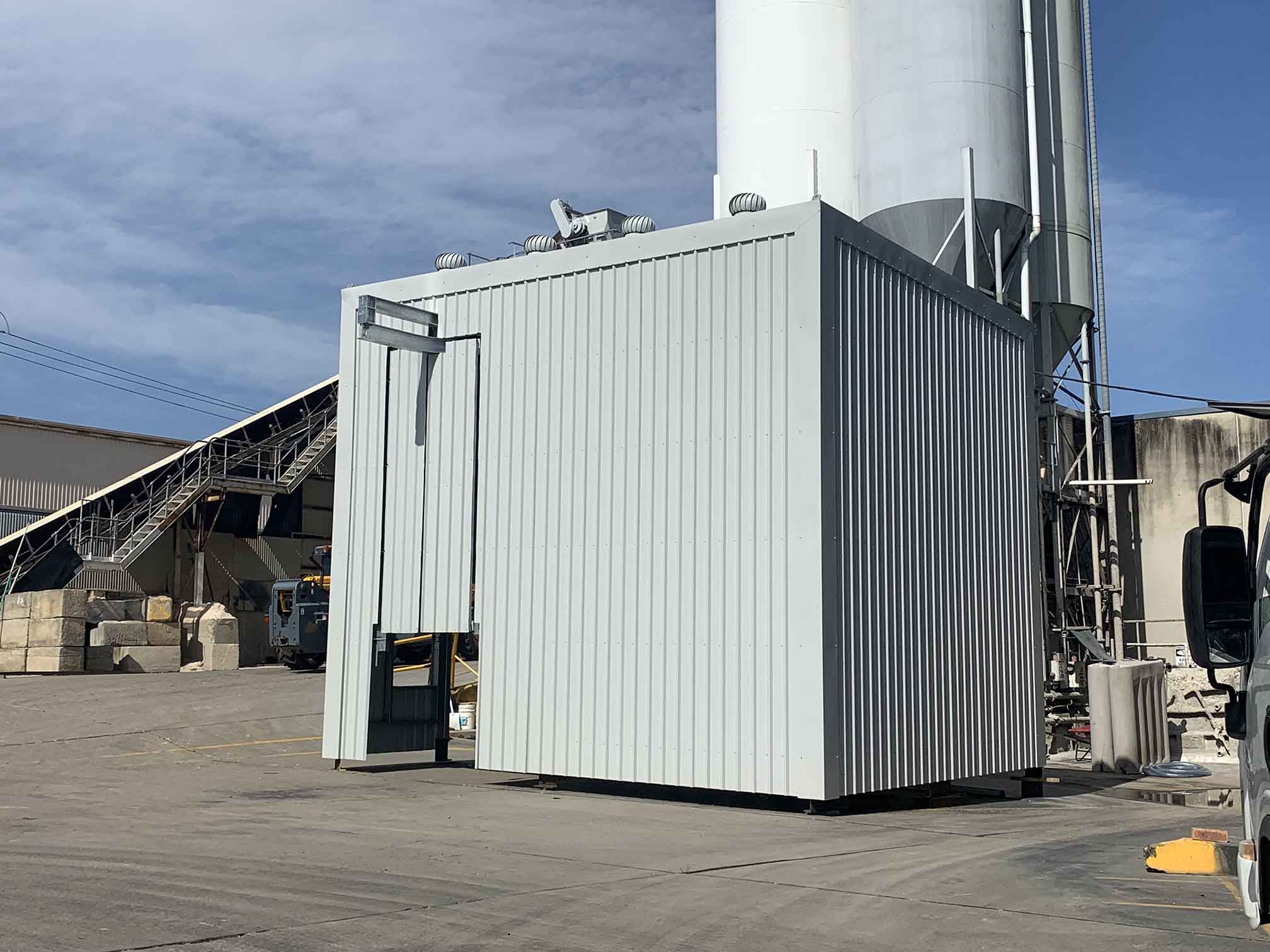 Metal-clad enclosure in an industrial yard beside a tall silo